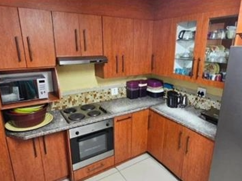 A functional kitchen featuring wood-look laminate cabinetry, granite countertops, a mosaic tile backsplash, and integrated appliances including an oven and hob.