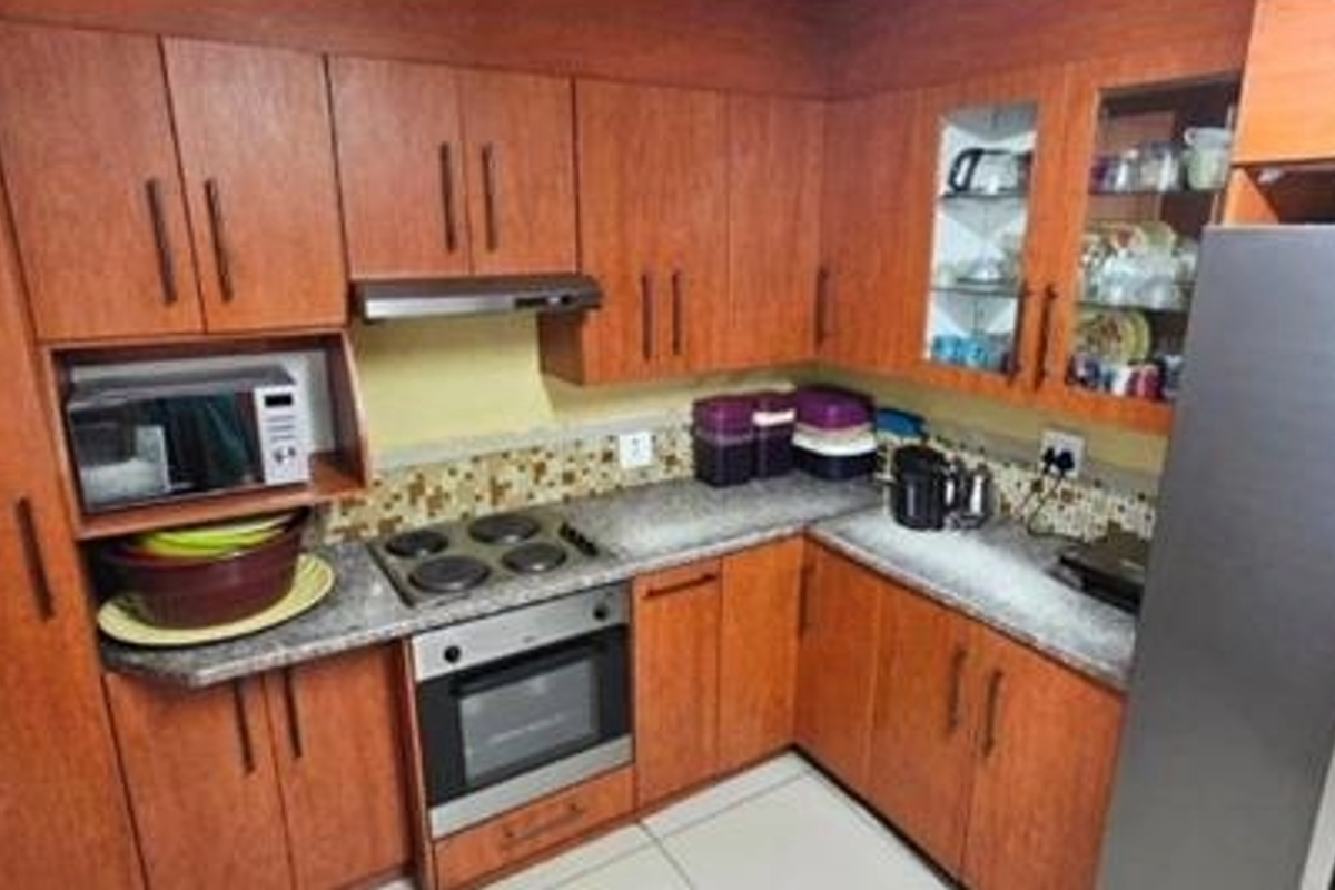 A functional kitchen featuring wood-look laminate cabinetry, granite countertops, a mosaic tile backsplash, and integrated appliances including an oven and hob.