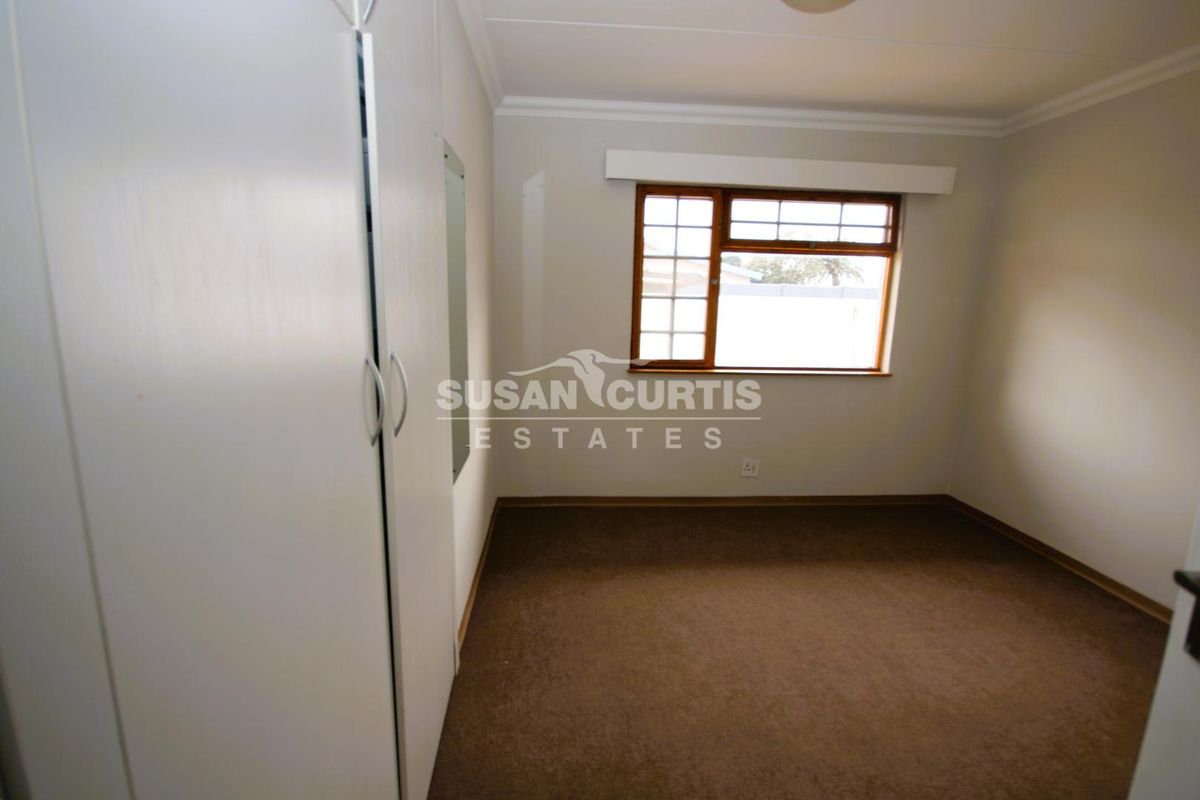 A clean, empty bedroom featuring built-in cupboards, carpeted flooring, and a wooden window frame, offering a neutral space ready for personalization.