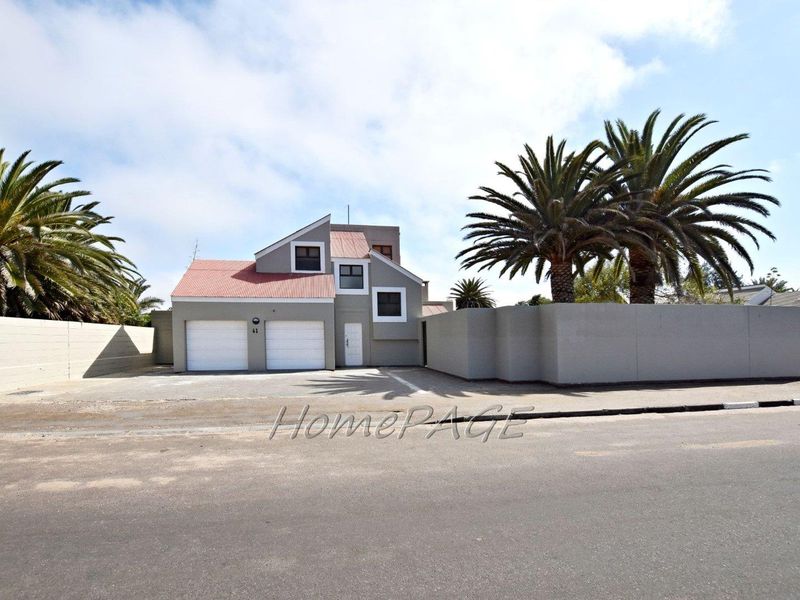 Front elevation of a multi-level house featuring a double garage, tiled roof, and a secure boundary wall with a paved driveway.