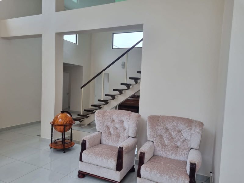 Spacious living area featuring double volume ceilings, tiled flooring, and an open staircase with a modern handrail.