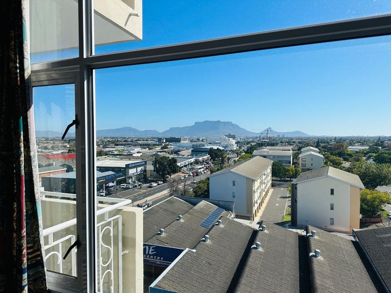 Elevated urban view overlooking the surrounding neighbourhood and distant mountain range, framed by an apartment window.