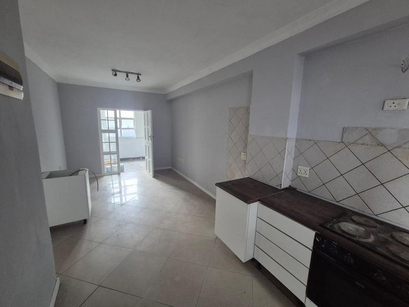 An open-plan kitchen and living area featuring tiled floors, built-in cabinetry, and an integrated oven, leading out to a balcony.