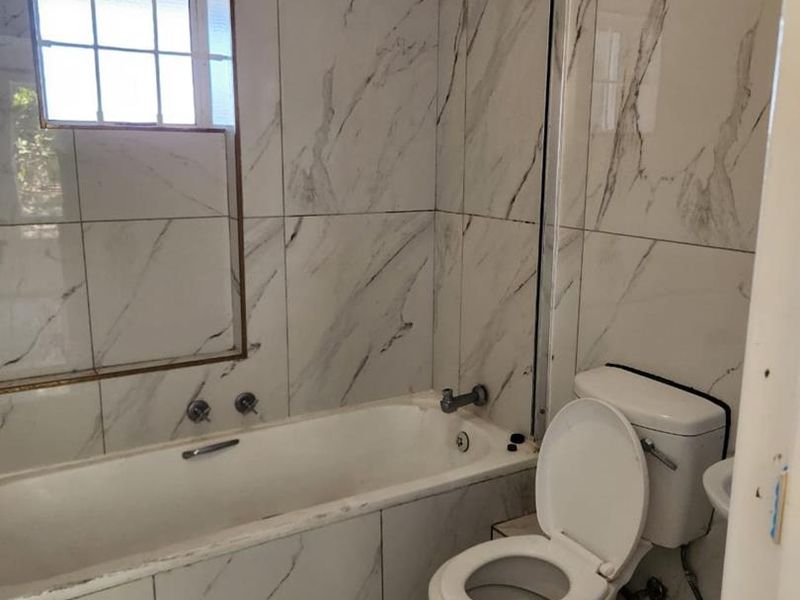 A bathroom featuring marble-look wall tiles, a bathtub with a shower head, and a toilet. The space is clean but shows minor wear.