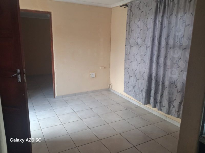 An empty bedroom featuring neutral tiled flooring and plain walls, providing a blank canvas for personalization.