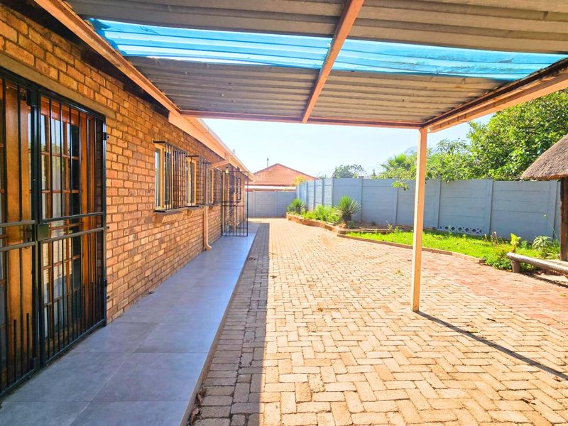 A spacious outdoor area featuring a paved driveway, a covered carport structure, and a brick-walled exterior with secure access points.