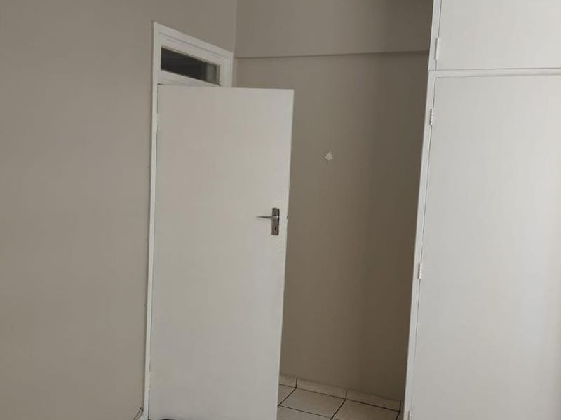 An empty bedroom featuring neutral wall paint, tiled flooring, and built-in storage cupboards.