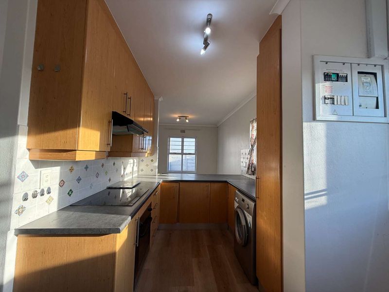 A functional kitchen featuring wood-finish cabinetry, dark laminate countertops, built-in appliances, and an integrated washing machine, offering a practical layout with natural light.