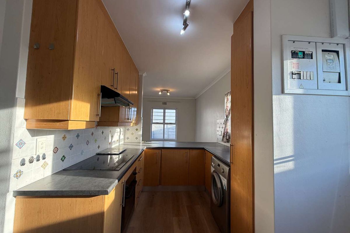 A functional kitchen featuring wood-finish cabinetry, dark laminate countertops, built-in appliances, and an integrated washing machine, offering a practical layout with natural light.