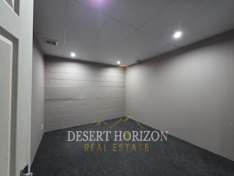 An empty utility or storage room featuring a drop ceiling, recessed lighting, and durable carpet flooring with a painted cinder block accent wall.