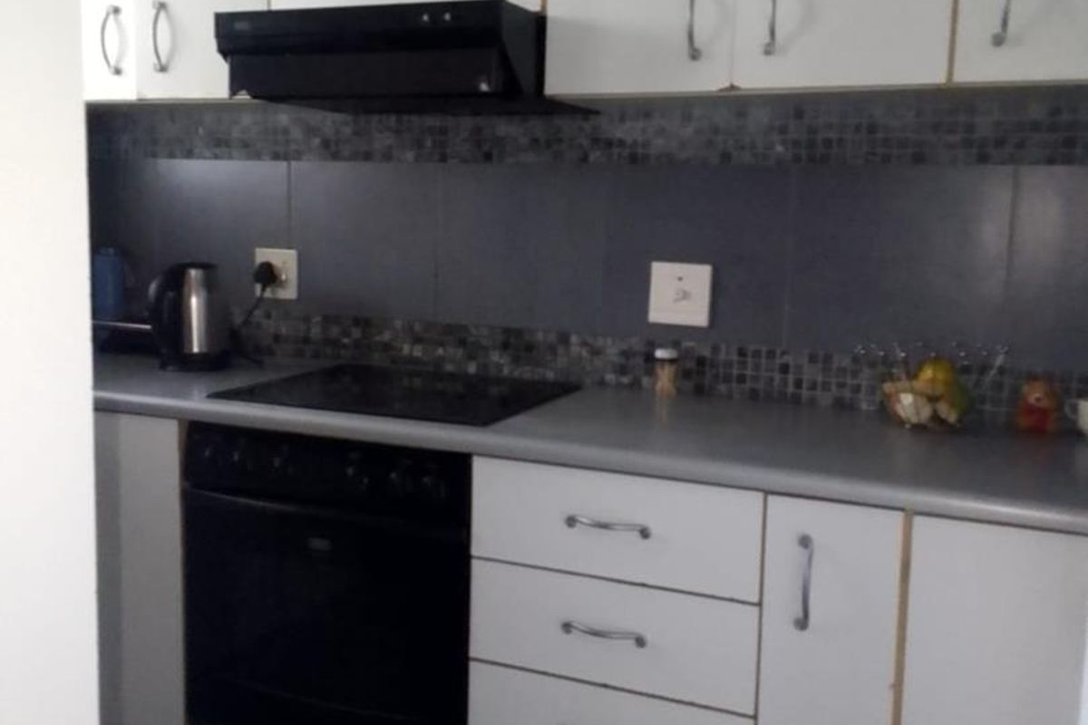 Compact kitchen featuring white cabinetry, a dark tiled backsplash, built-in oven, and electric hob with an extractor fan.