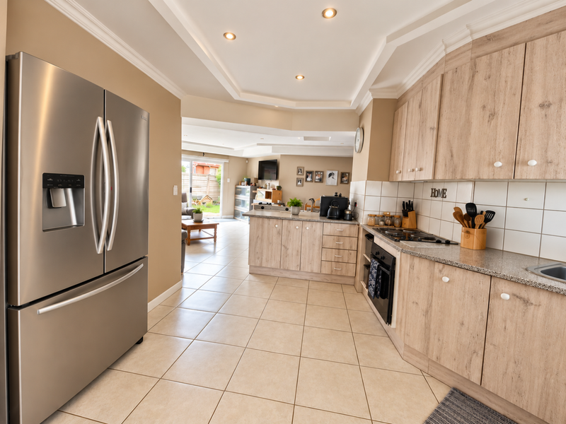 Open-plan kitchen featuring light wood-grain cabinetry, granite countertops, built-in oven, and gas hob, flowing seamlessly into a bright living area with garden access.