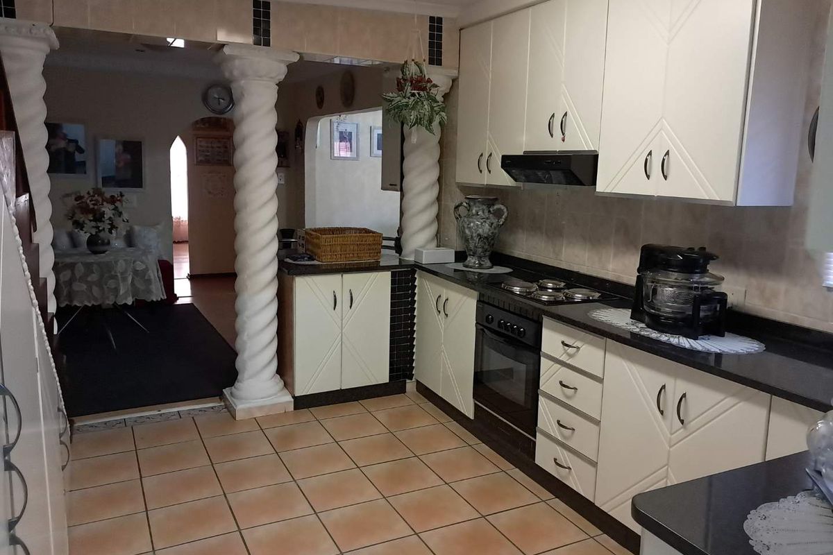 A functional kitchen featuring built-in cabinetry, integrated oven and hob, extractor fan, and tiled flooring, with decorative columns opening into the adjacent living area.