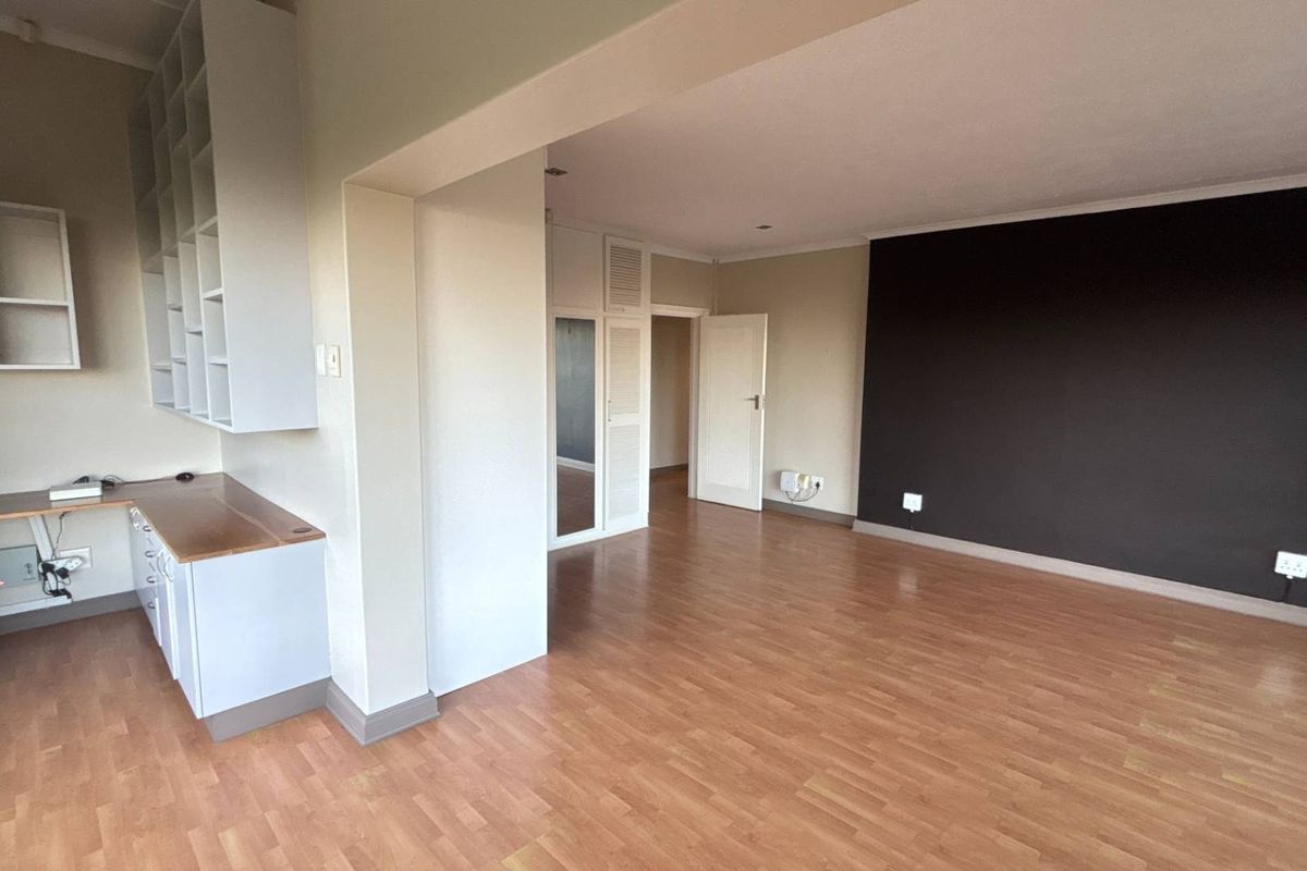 A spacious room featuring laminate flooring, built-in shelving, a desk area, and integrated storage cupboards, offering a versatile layout for living or office use.