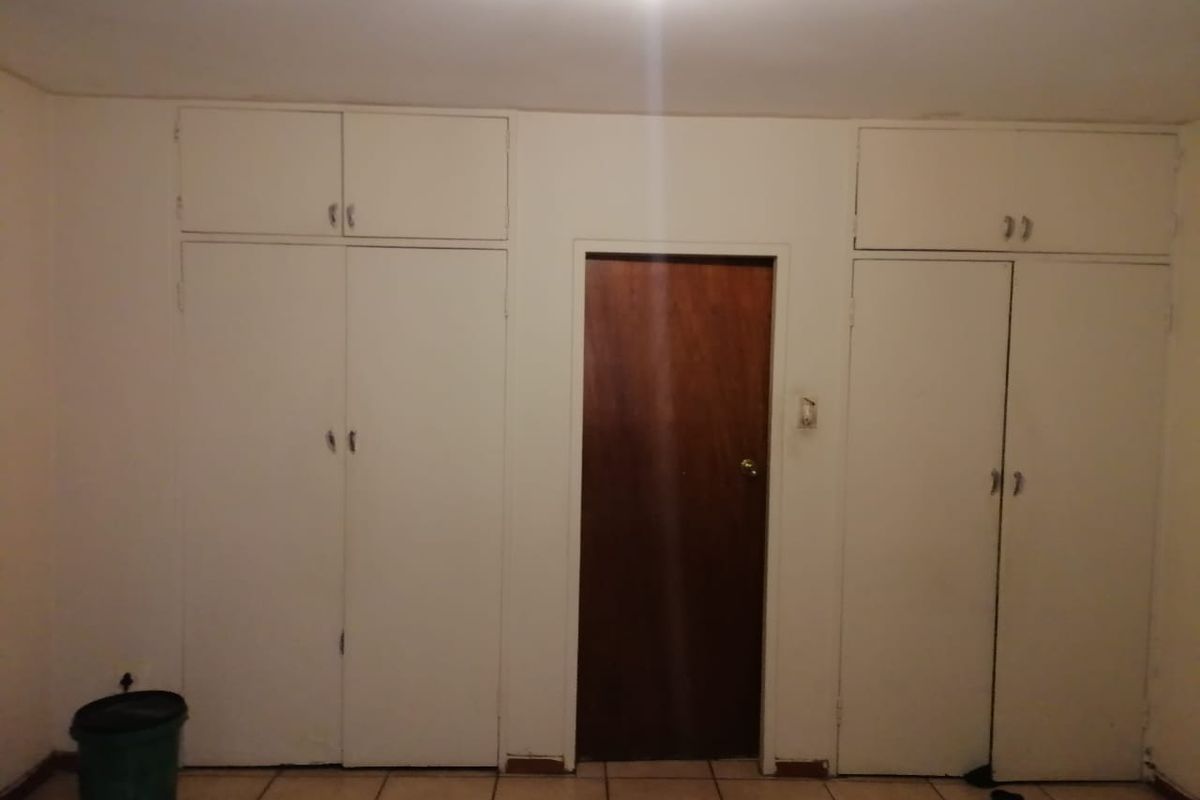 A bedroom featuring built-in cupboards with overhead storage and tiled flooring, presenting a blank canvas for potential renovation or interior design updates.
