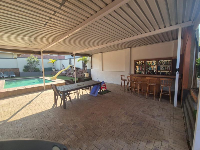 Spacious covered patio area featuring a built-in bar, paved flooring, and direct access to an outdoor swimming pool.