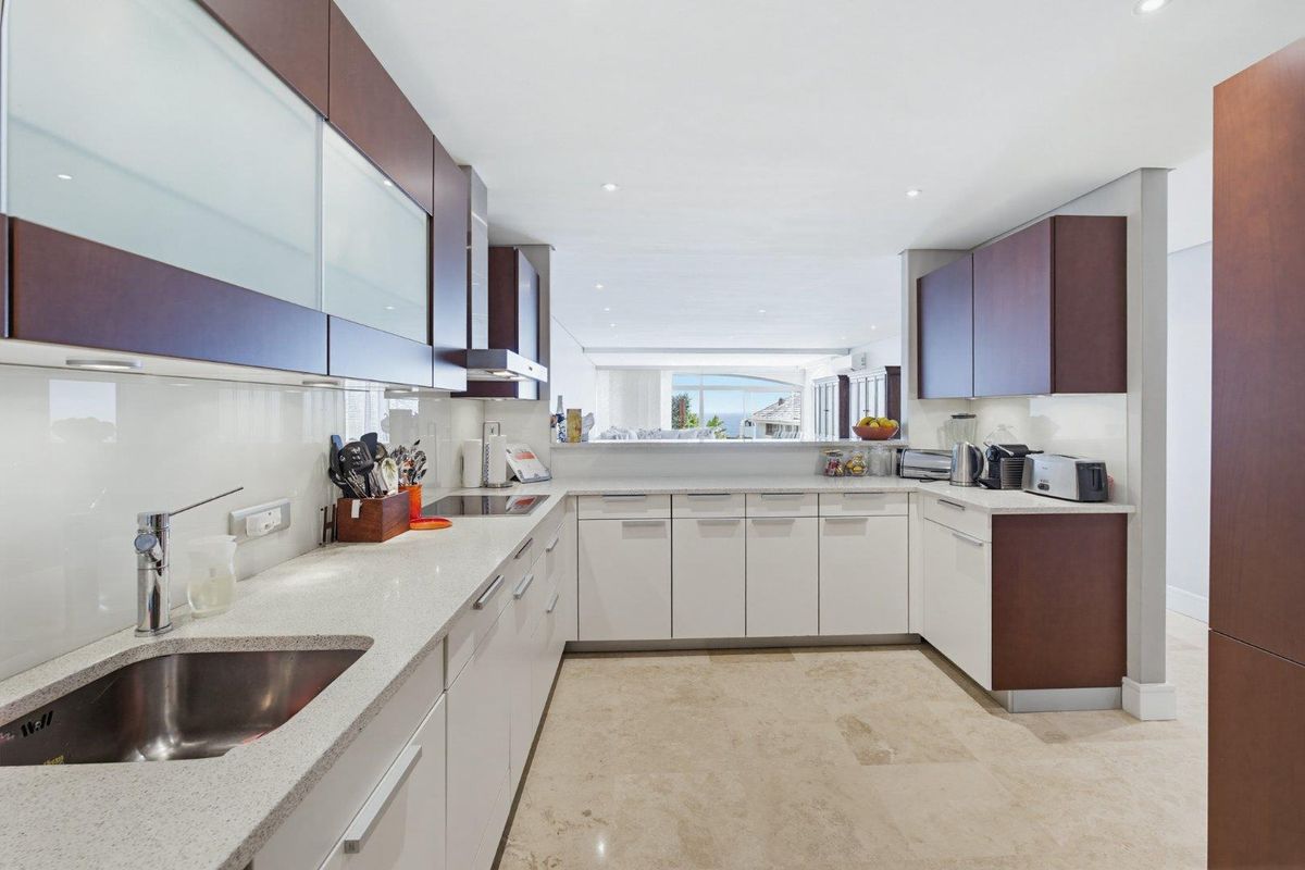Modern kitchen featuring sleek two-tone cabinetry, stone countertops, integrated appliances, and high-quality stone flooring, with an open-plan layout overlooking the living area.