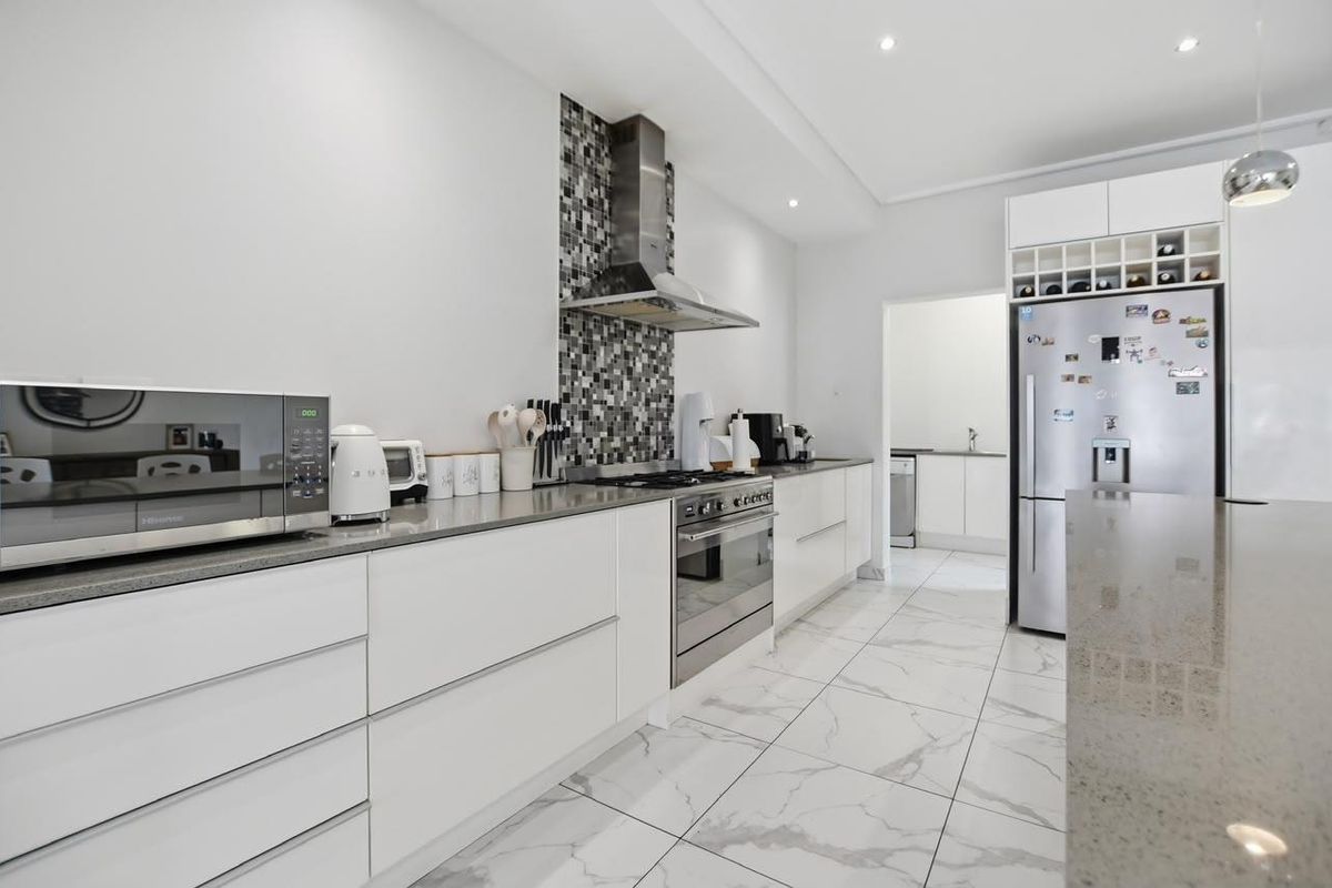 Modern kitchen featuring stone countertops, stainless steel appliances, mosaic tile splashback, and marble-look floor tiles with an adjacent scullery area.