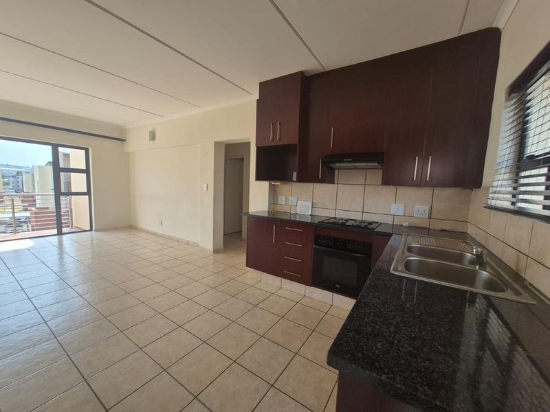 Open-plan kitchen and living area featuring dark wood cabinetry, granite countertops, built-in oven, hob, and tiled flooring with access to a balcony.