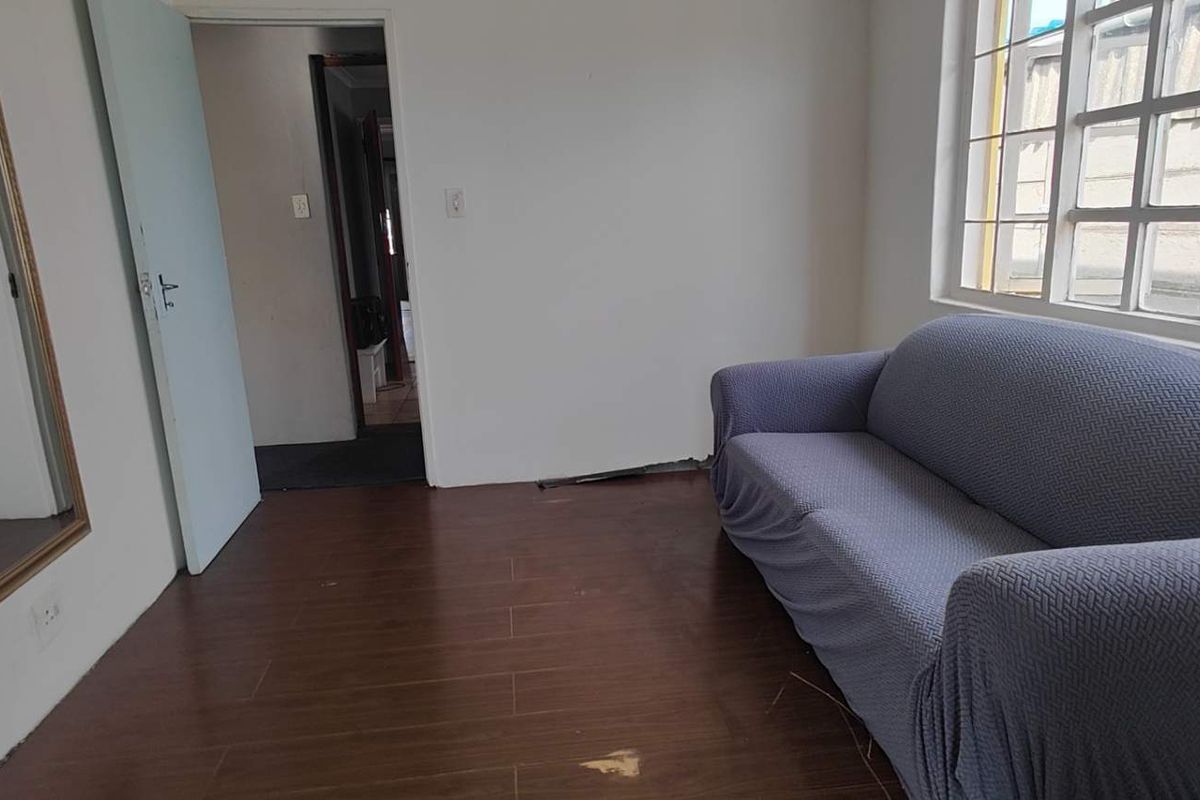 A living room featuring dark laminate flooring and a large grid-pattern window, showing signs of wear on the floor surface.