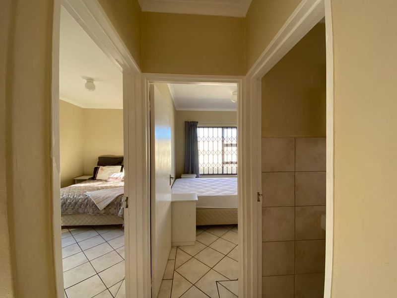 A view from a central hallway looking into two bedrooms, featuring ceramic floor tiles and neutral wall finishes.