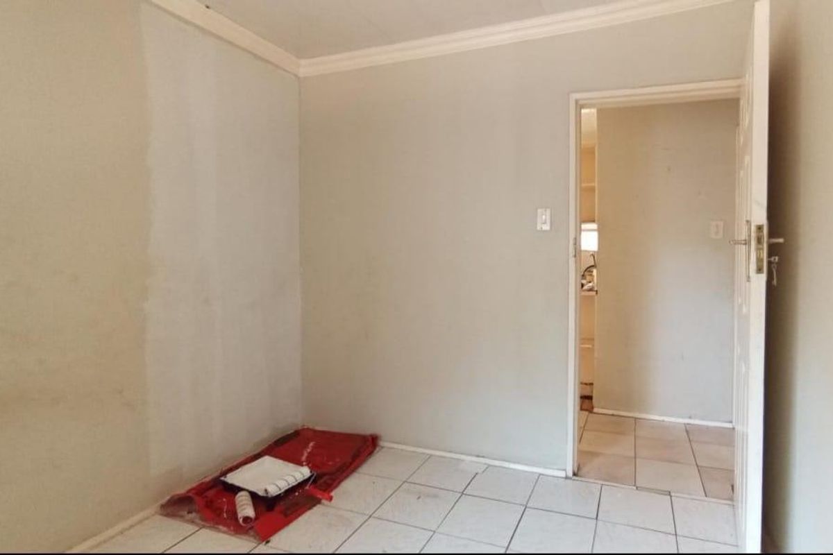 A small, empty bedroom featuring tiled flooring and a doorway leading to an adjacent space, currently undergoing interior painting.