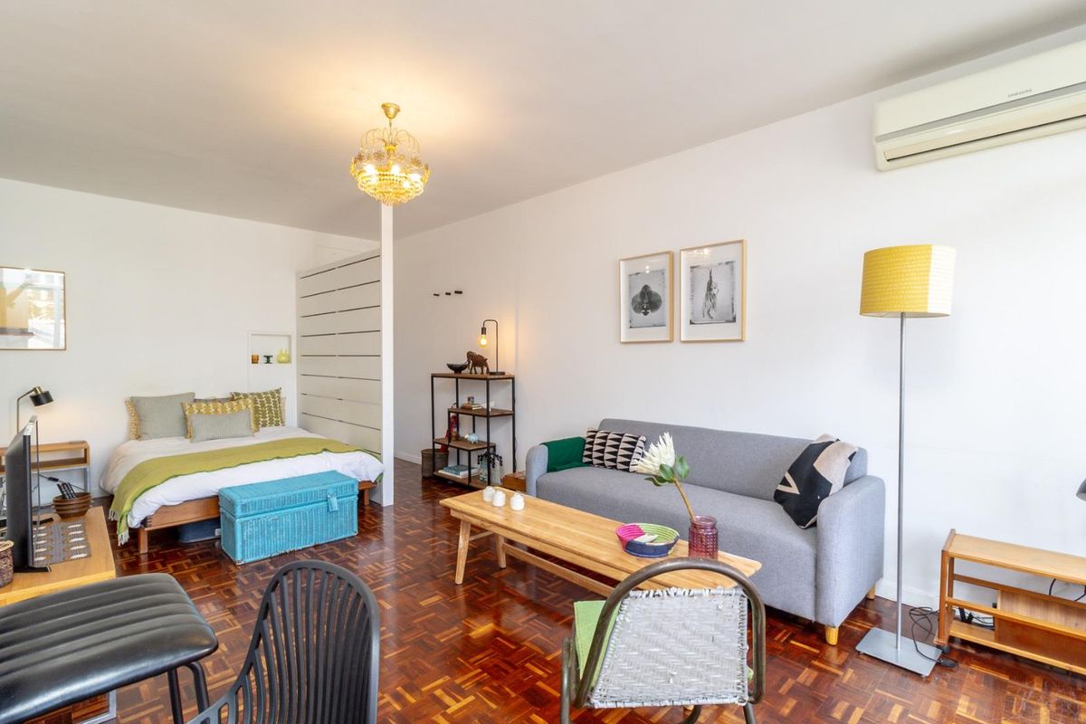 An open-plan studio apartment featuring warm parquet flooring, a wall-mounted air conditioning unit, and a functional room divider separating the sleeping and living areas.
