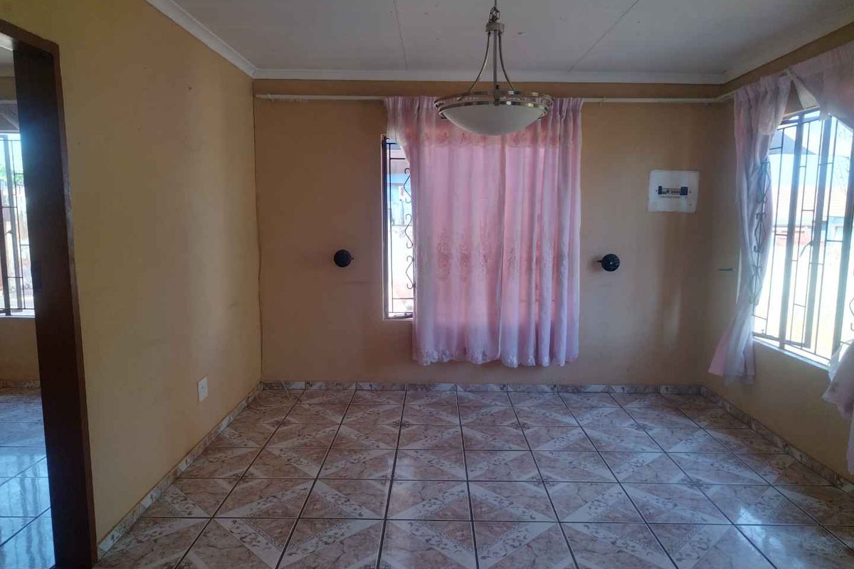 An empty living room featuring tiled flooring, a central pendant light fixture, and security bars on the windows.