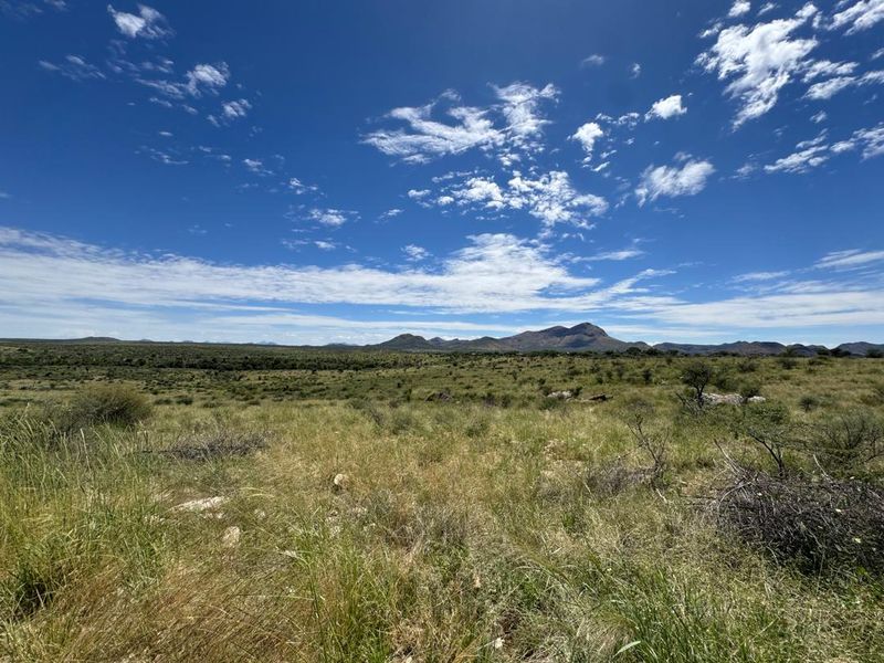 Expansive landscape view featuring natural veld and distant mountain ranges under a clear blue sky.