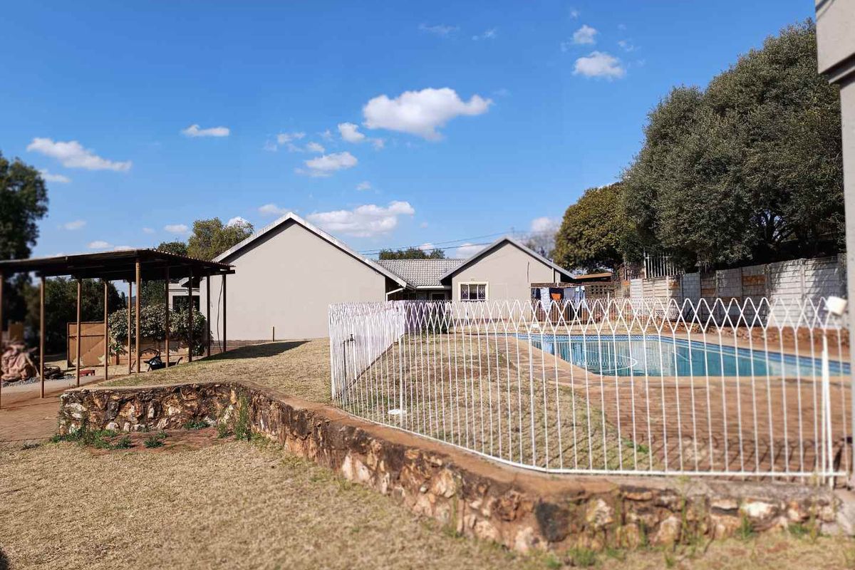 Rear exterior view featuring a swimming pool, stone retaining wall, and a covered patio area set within a spacious garden.