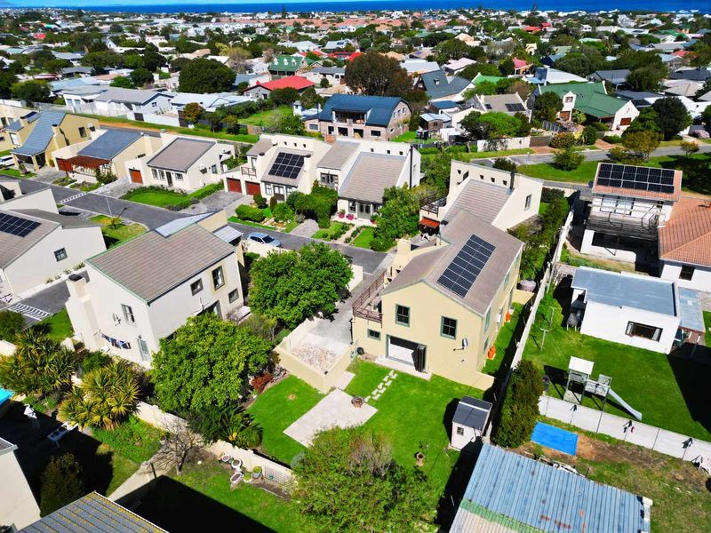 Aerial view of a residential property featuring a tiled roof with solar panels, a private garden, and paved driveway within a suburban neighborhood.