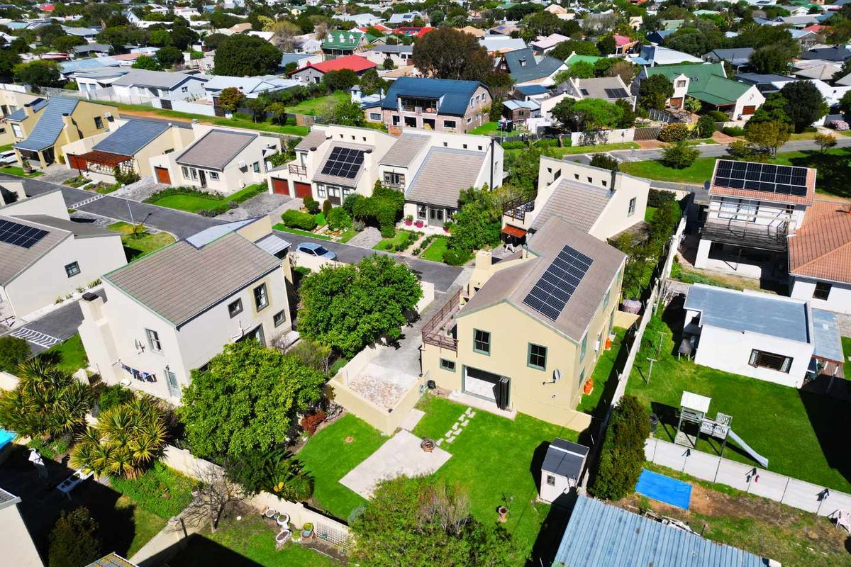 Aerial view of a residential property featuring a tiled roof with solar panels, a private garden, and paved driveway within a suburban neighborhood.