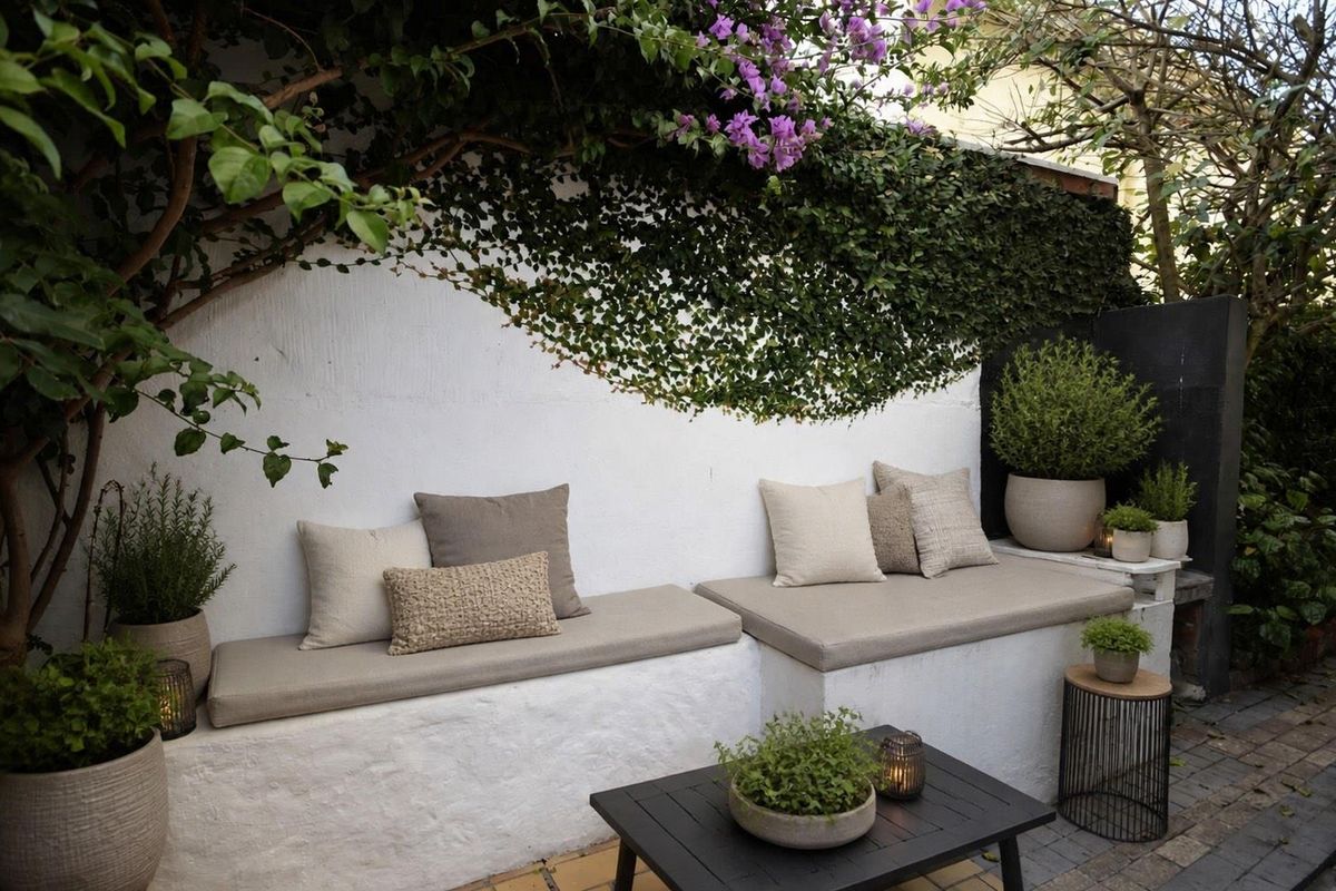 A charming outdoor patio area featuring built-in masonry bench seating and established climbing greenery against a white wall.