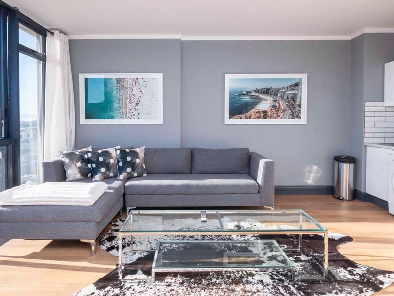 Modern open-plan living area featuring laminate flooring, floor-to-ceiling windows with natural light, and a compact kitchen with subway tile backsplash and integrated laundry.