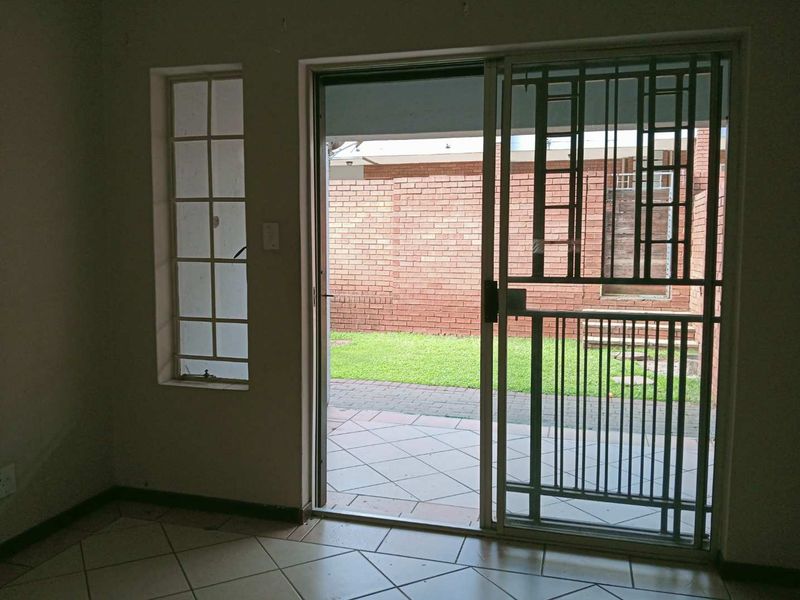 An empty living area featuring tiled flooring, a sliding glass door with a security gate, and direct access to a paved patio and garden.