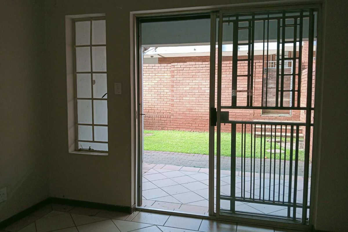 An empty living area featuring tiled flooring, a sliding glass door with a security gate, and direct access to a paved patio and garden.