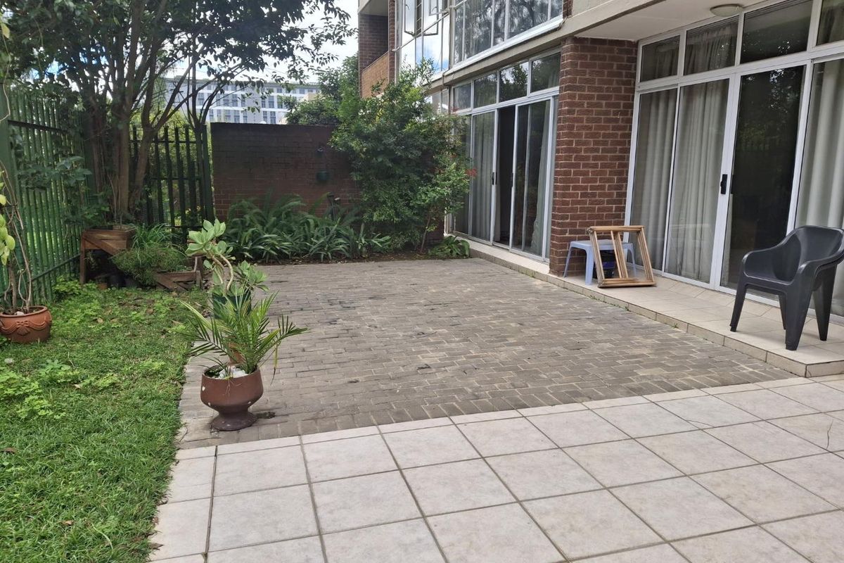 A private rear patio area featuring a combination of brick paving and tiled flooring, directly accessible from the apartment through sliding glass doors.