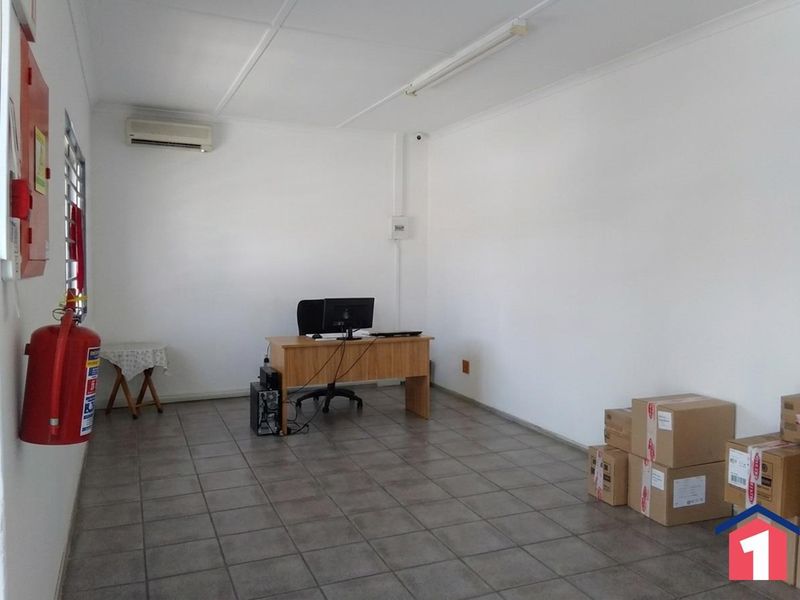 A functional office space featuring tiled flooring, a wall-mounted air conditioning unit, and essential fire safety equipment.