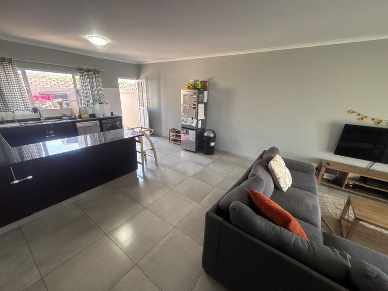 Open-plan living area featuring a kitchen with dark cabinetry and granite countertops, seamlessly flowing into the lounge space with neutral tiled flooring throughout.
