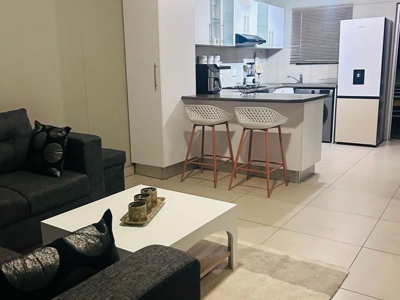 Open plan living area featuring a modern kitchen with white cabinetry, breakfast counter, and tiled flooring throughout the combined space.