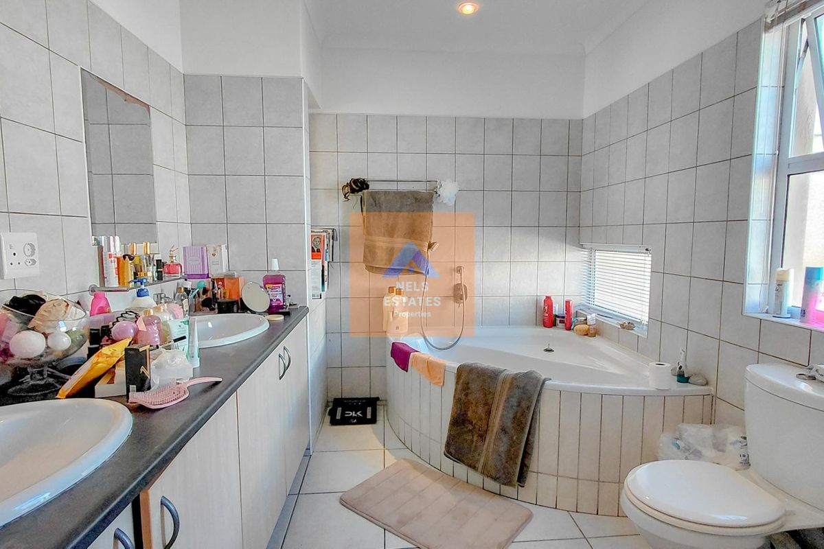 A functional bathroom featuring a corner bathtub, dual vanity with integrated sinks, and tiled wall finishes.