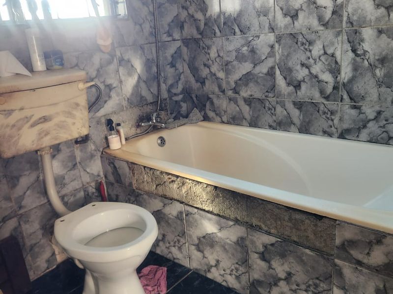 A functional bathroom featuring a bathtub, toilet, and marble-effect wall tiling. The space requires cosmetic updates and maintenance to improve its overall condition.