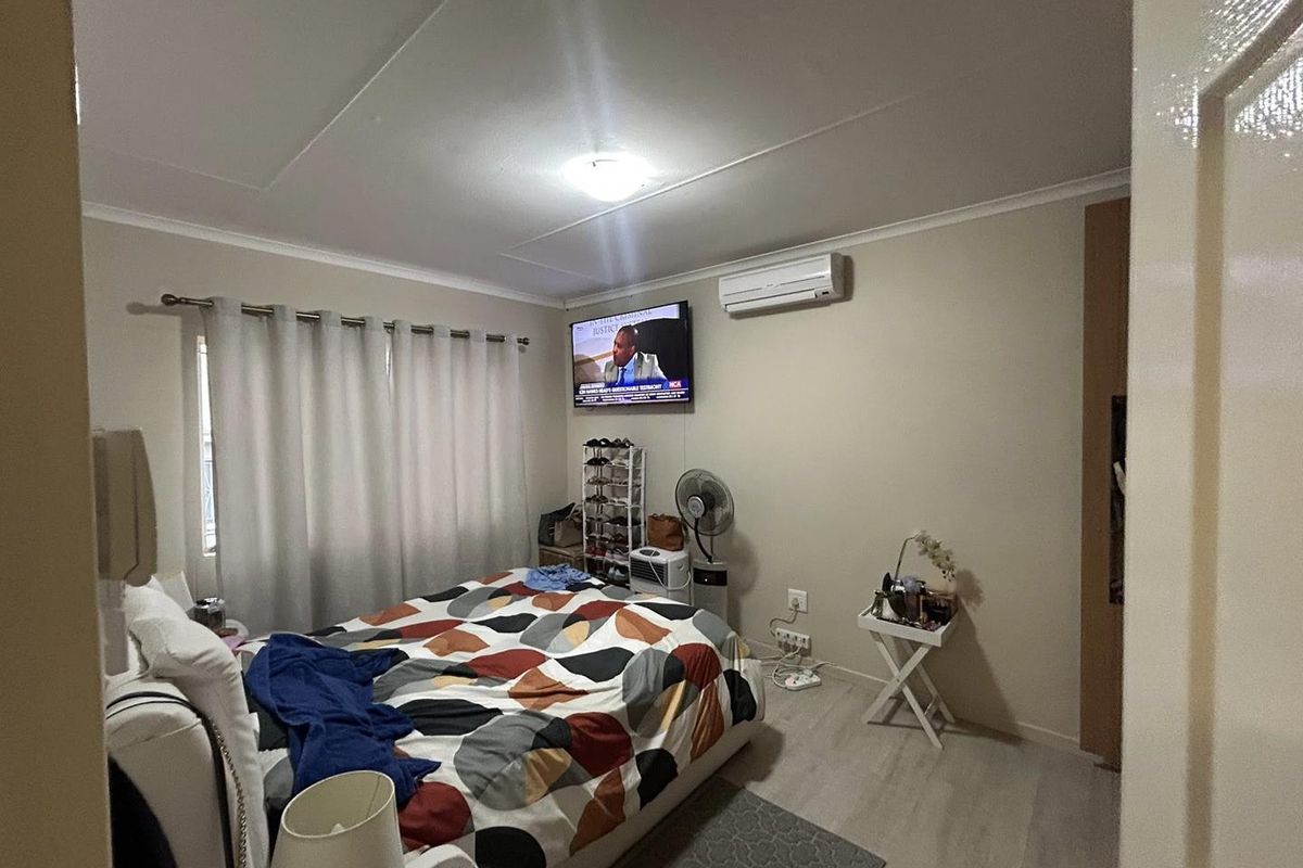 A bedroom featuring light-toned laminate flooring, a wall-mounted air conditioning unit, and built-in cupboard space.