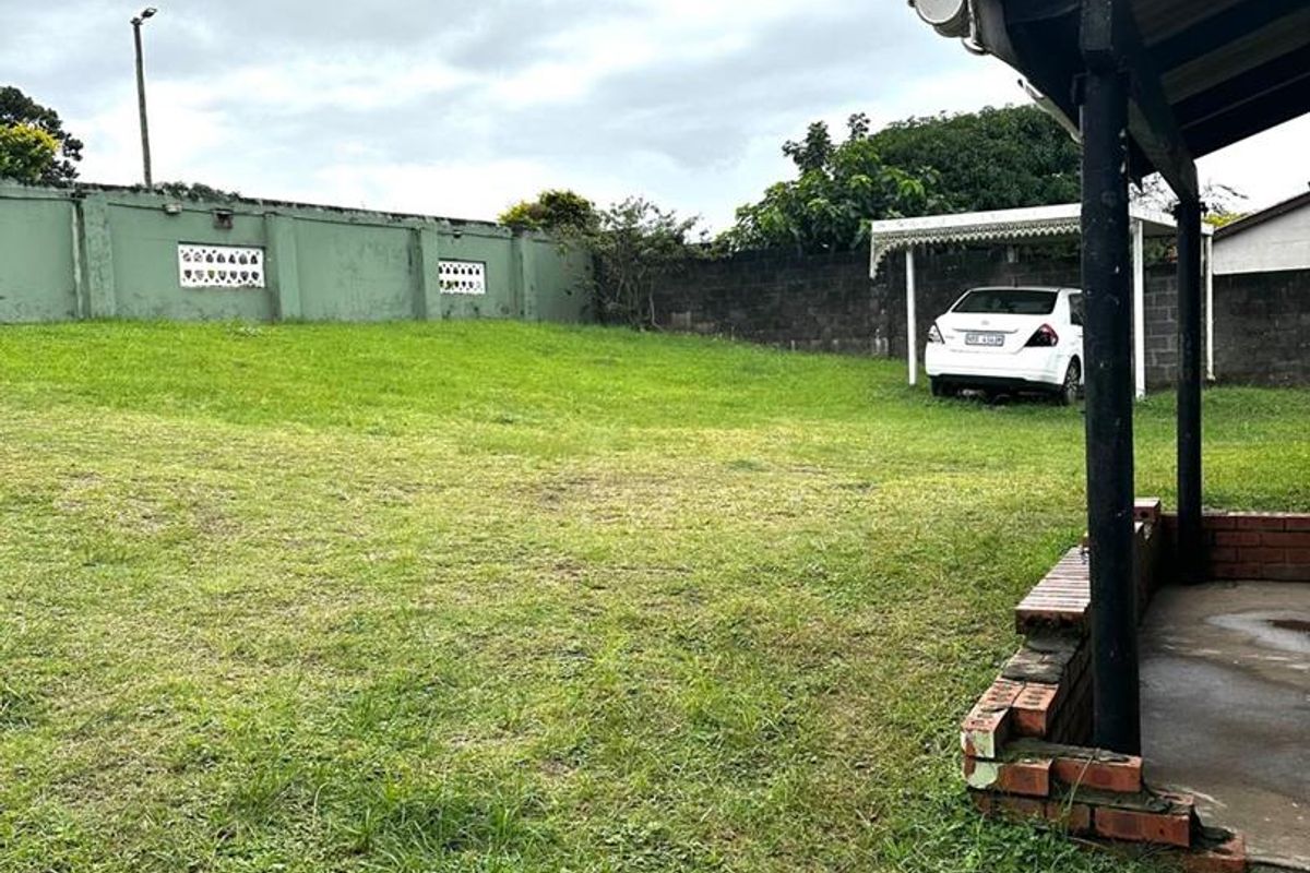 A spacious rear garden featuring a covered patio area, a carport structure, and a perimeter boundary wall.