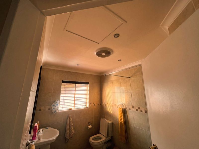 A functional bathroom featuring tiled walls, a pedestal basin, a toilet, and a shower area with an extractor fan.