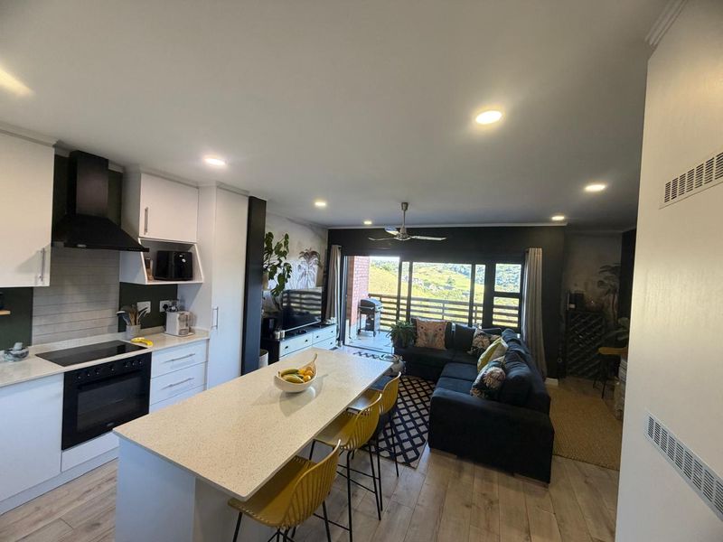 Modern open-plan living area featuring a contemporary kitchen with a central island, sleek cabinetry, and seamless flow to a balcony with scenic views.