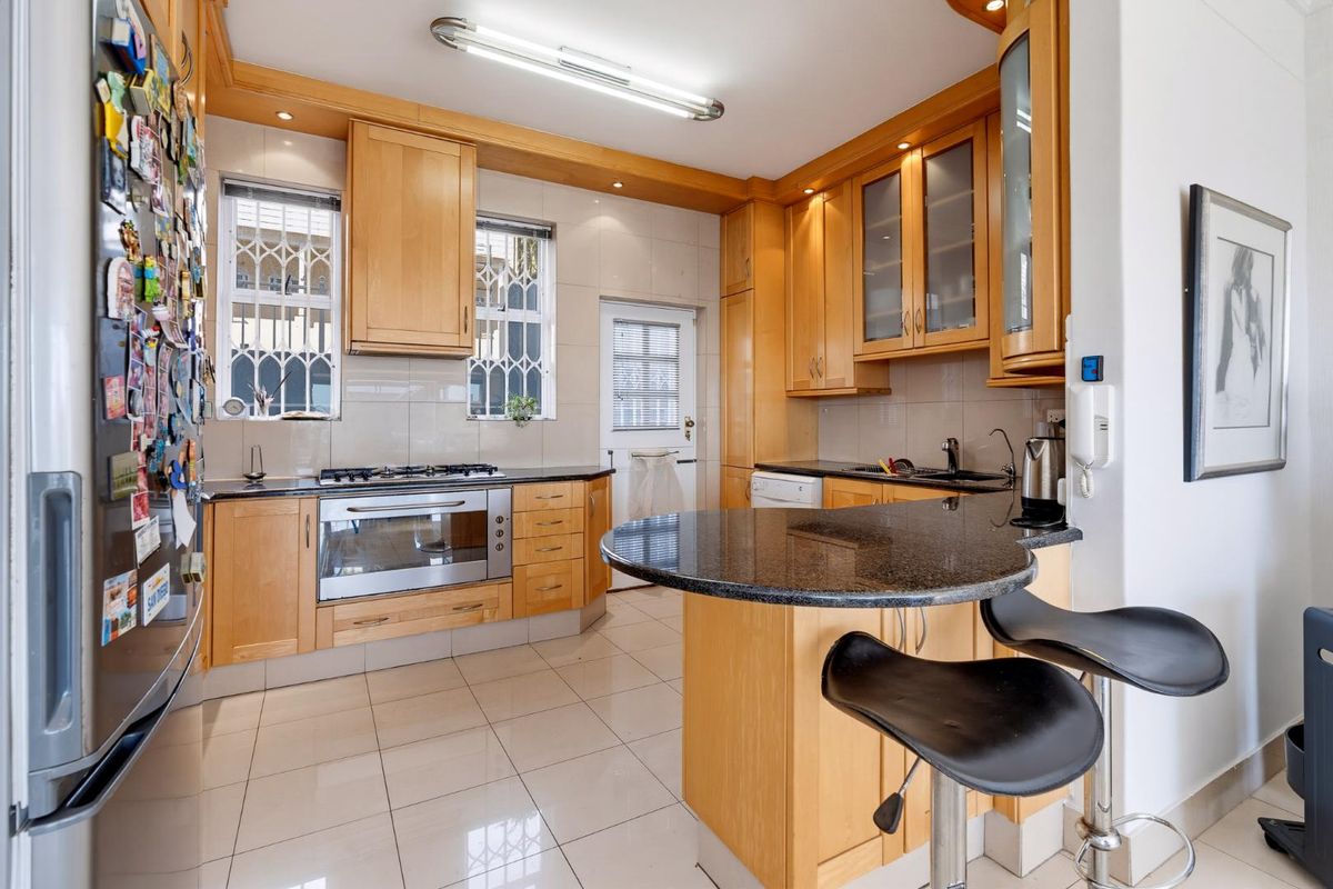 A functional kitchen featuring light wood cabinetry, granite countertops, a breakfast bar, and integrated gas cooking appliances with tiled flooring throughout.