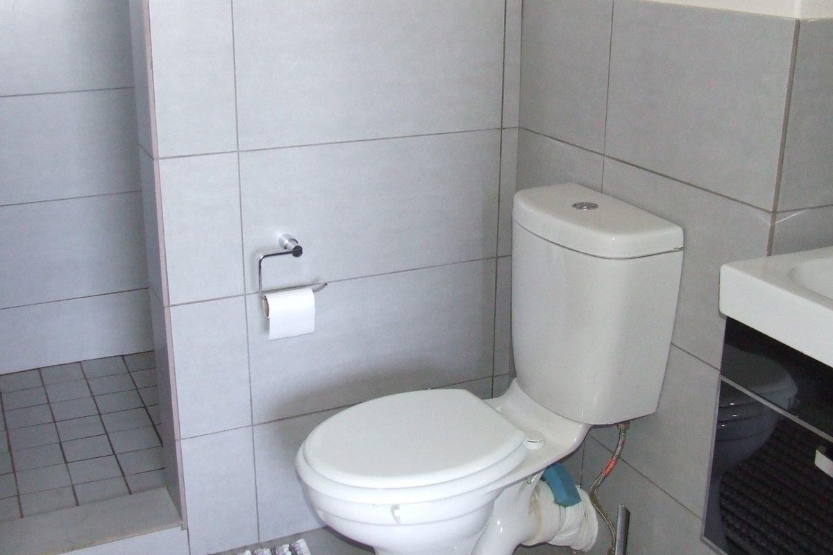 A functional bathroom featuring grey wall tiling, a white toilet, and a walk-in shower area with matching floor tiles.