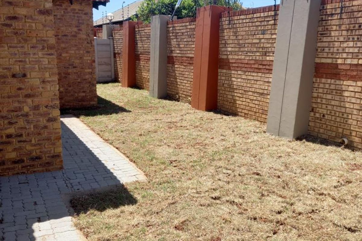 A private rear garden area featuring a paved walkway, perimeter brick walling with integrated security fencing, and established boundary pillars.