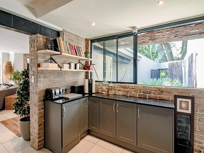 A modern kitchen area featuring dark cabinetry, black stone countertops, exposed brick walls, and large sliding windows overlooking the garden.
